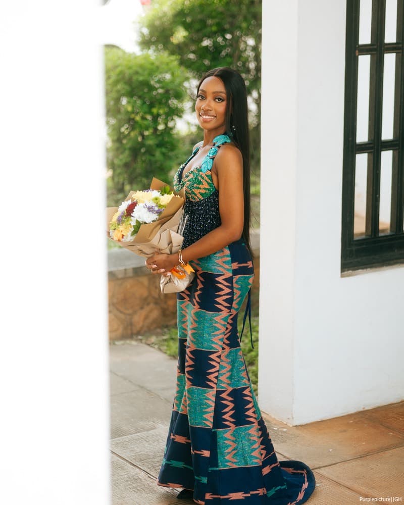 Graduate in a kente gown holding flowers