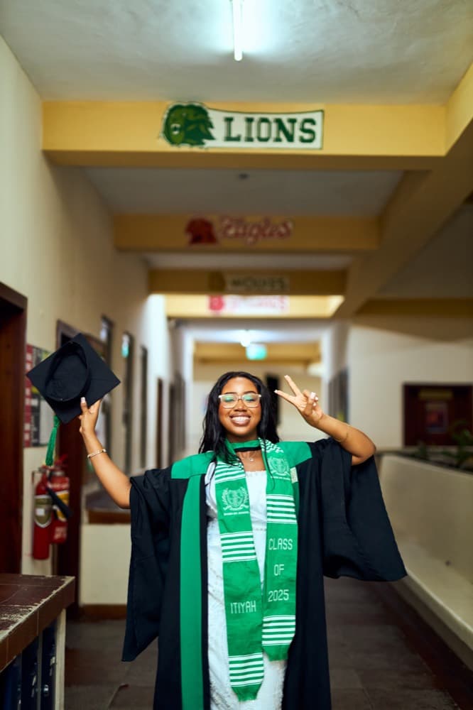 Graduate holding a mortarboard in a school hallway